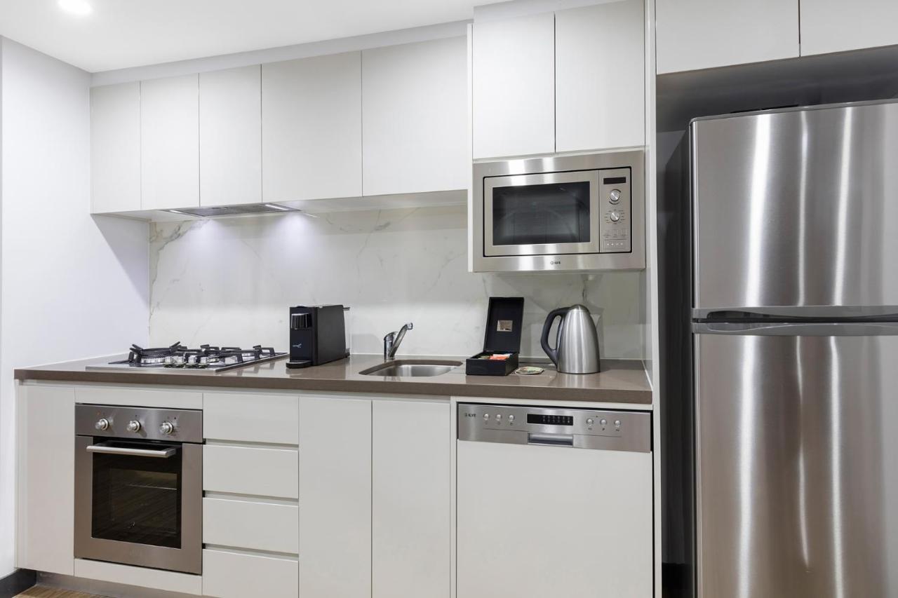 Meriton Suites Bondi Junction Sydney Exterior foto The photo shows a modern kitchen with a sleek, minimalist design. It features white cabinetry and a countertop that blends with the overall aesthetic. 

Key elements include:

- A stainless steel refrigerator on the right.
- An oven with a gas cookto