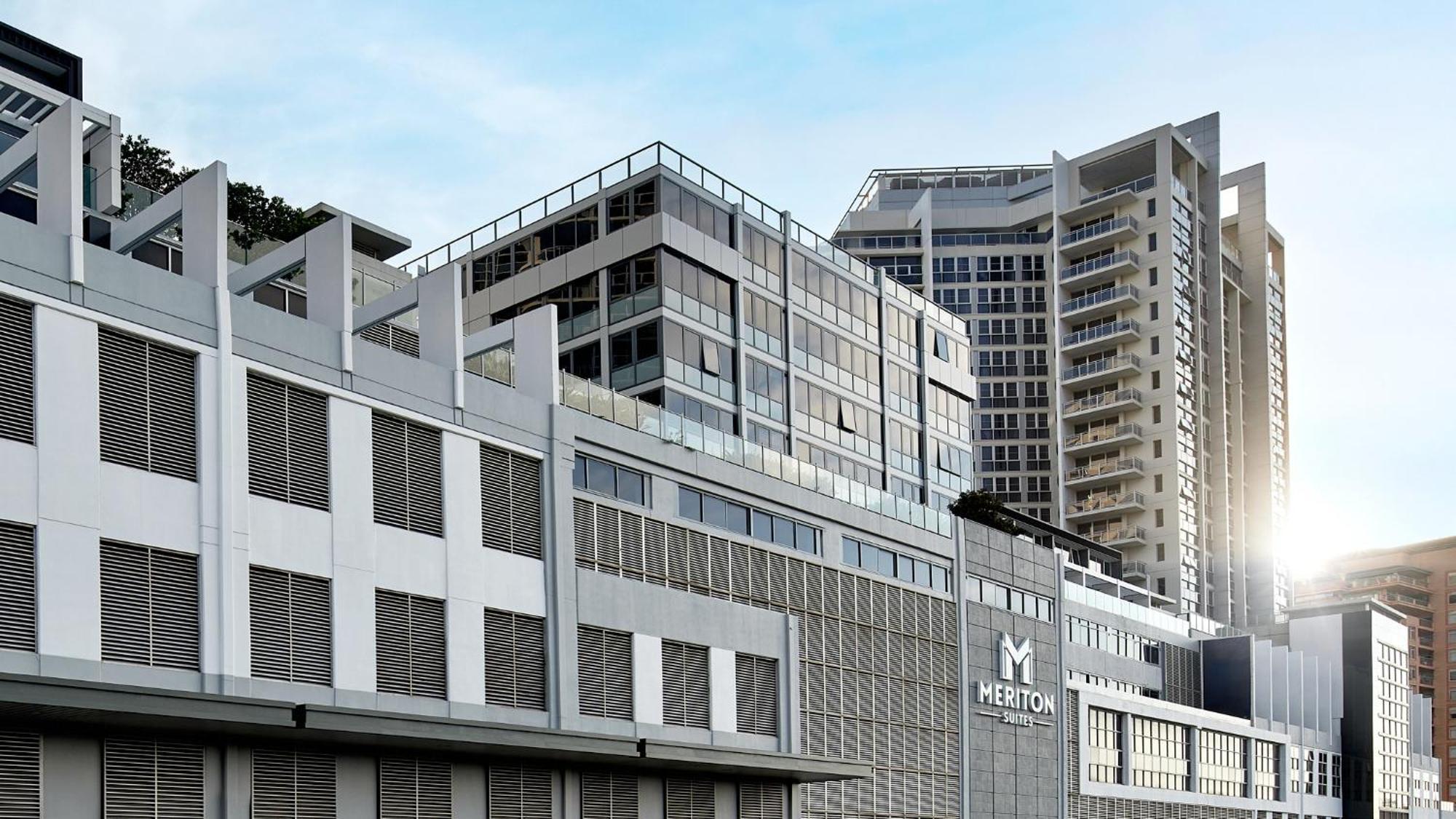 Meriton Suites Bondi Junction Sydney Exterior foto The image shows a modern urban building or complex. The structure features a combination of glass and concrete elements, showcasing contemporary architectural design. The foreground has a lower section that appears to be a podium or base with a textu